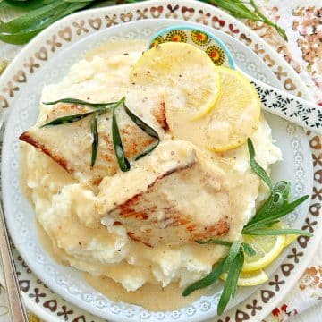 chicken tarragon plated with fresh tarragon, lemon slices and sauce on a bed of mashed potatoes