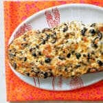garlic bread smothered with olives and cheese on a platter