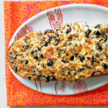 garlic bread smothered with olives and cheese on a platter