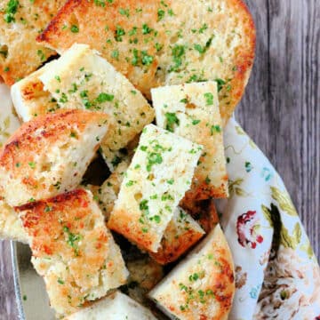 sliced garlic bread on a platter and garnished with fresh chopped parsley