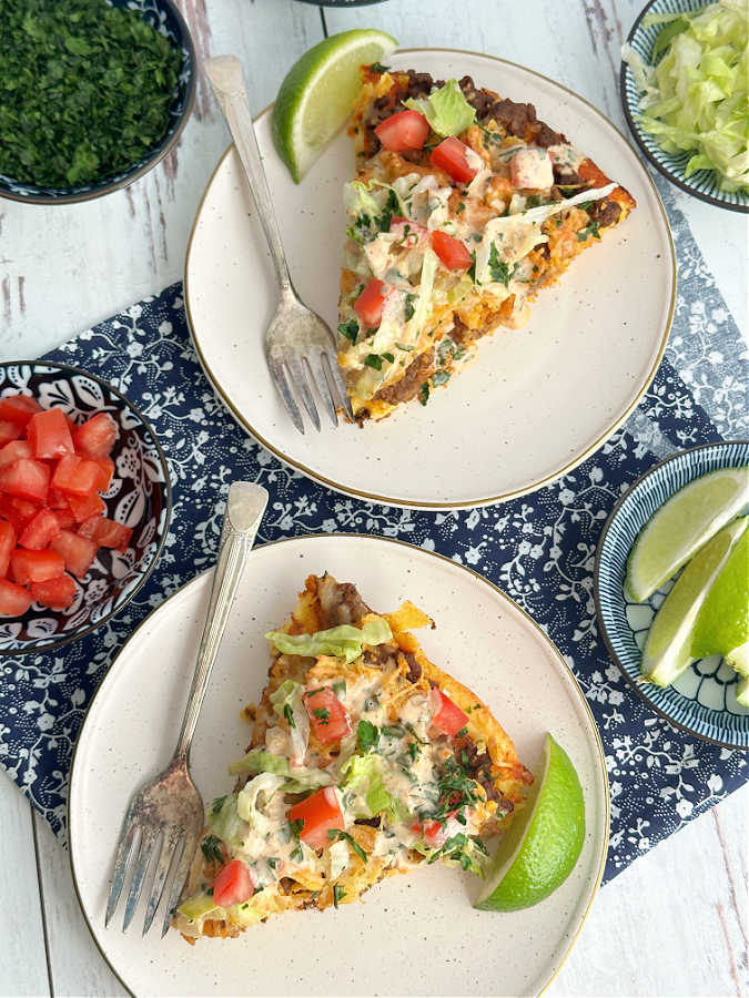 overhead shot of two styled plates with slices of taco pizza garnished with toppings and each with a lime slice on the side