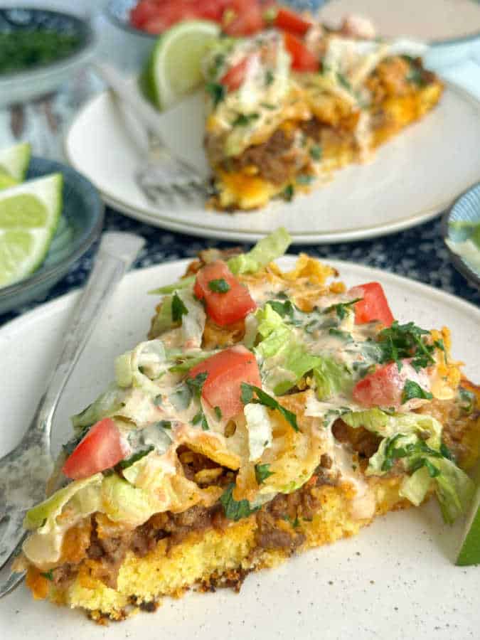 Two slices of taco pizza topped with shredded lettuce, diced tomatoes and chipotle Ranch dressing