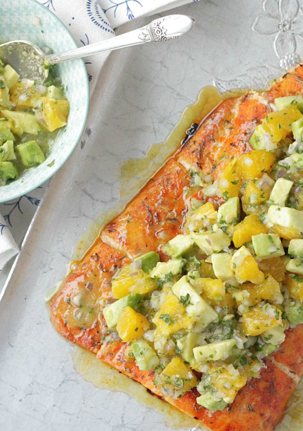 top view of whole piece of citrus salmon on a silver tray topped with the avocado and orange salsa