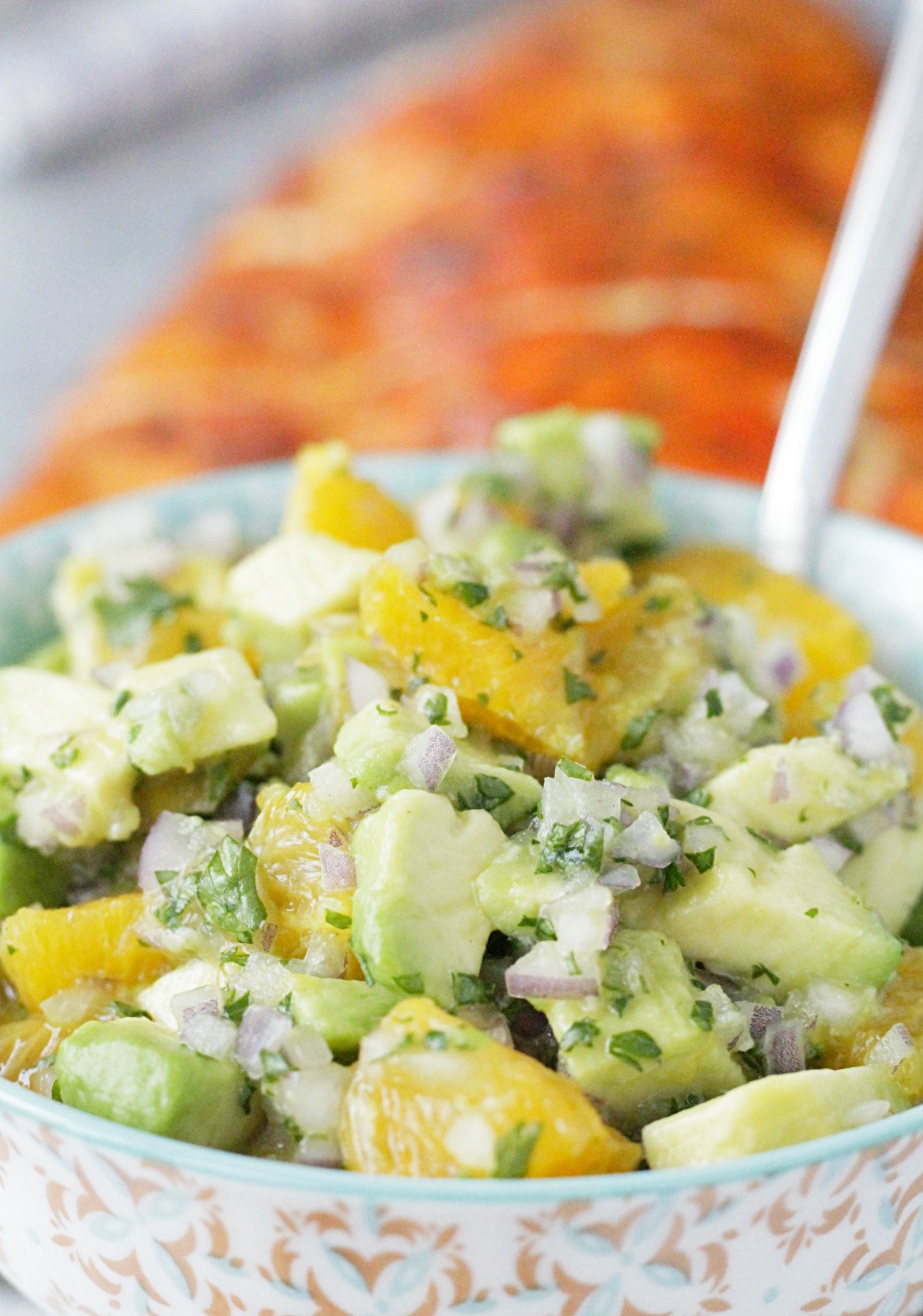 close up view of bowl of avocado and orange salsa with salmon in the background