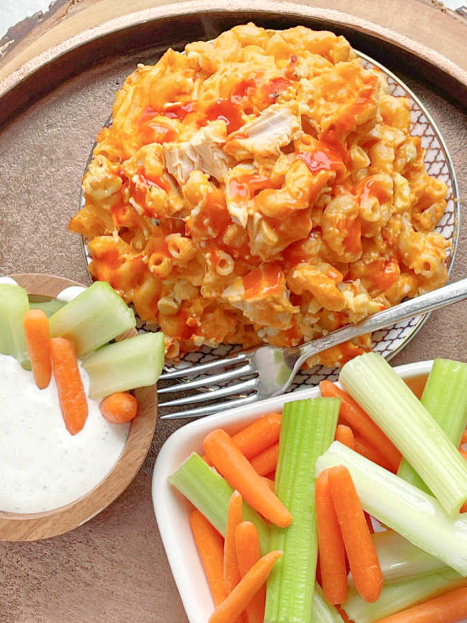 a dish of buffalo chicken mac and cheese served alongside a plate of celery and carrots with Ranch dressing to dip