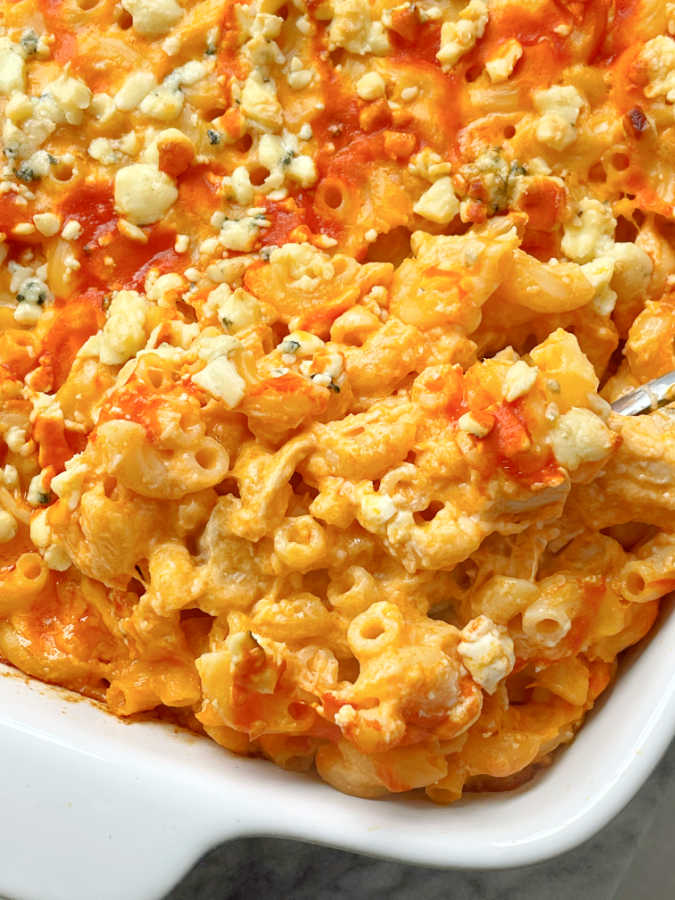 using a spoon to serve from a casserole dish of buffalo chicken mac and cheese