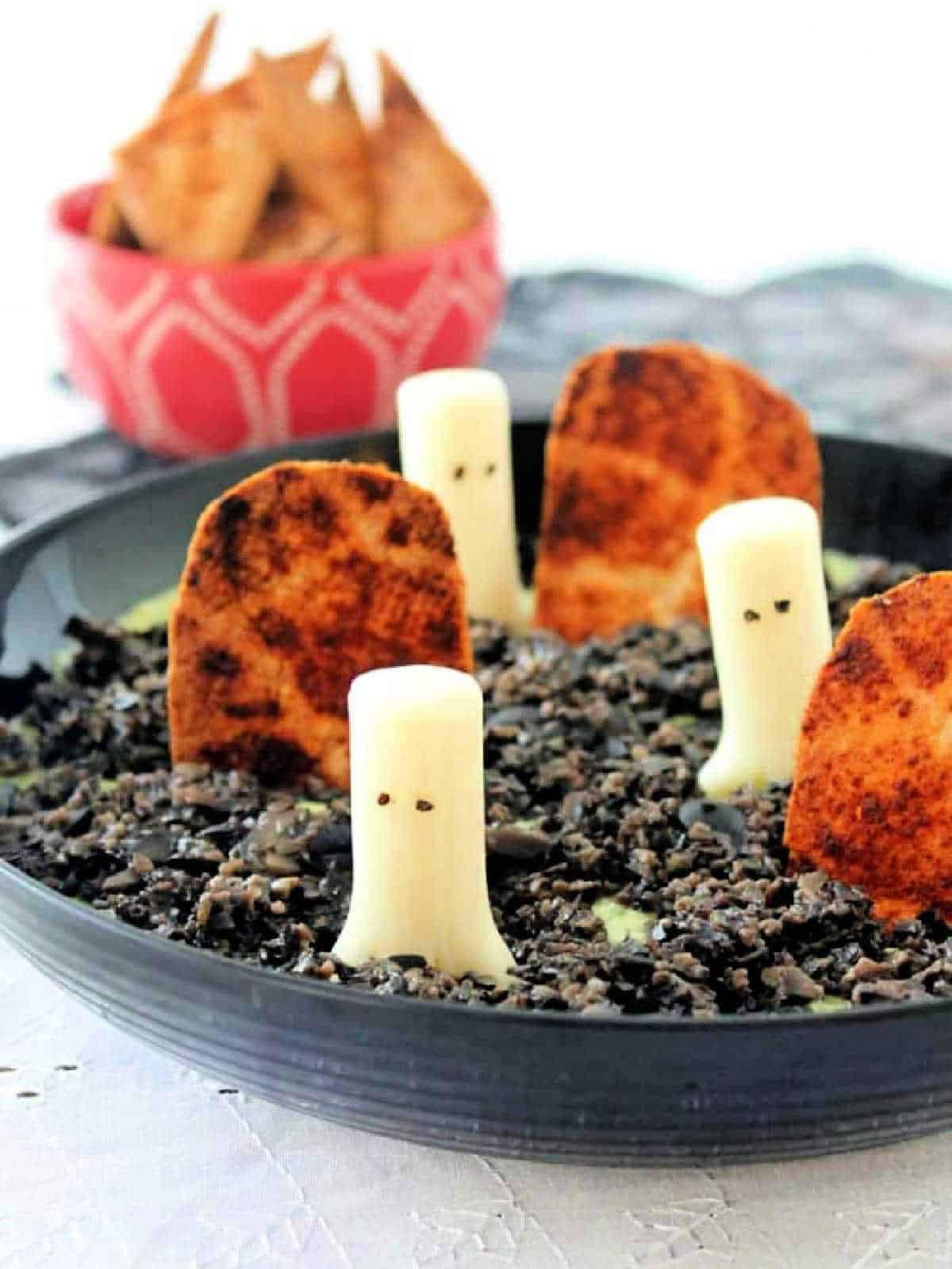shallow black bowl with halloween ghost in the graveyard dip and a red bowl with chips for dipping