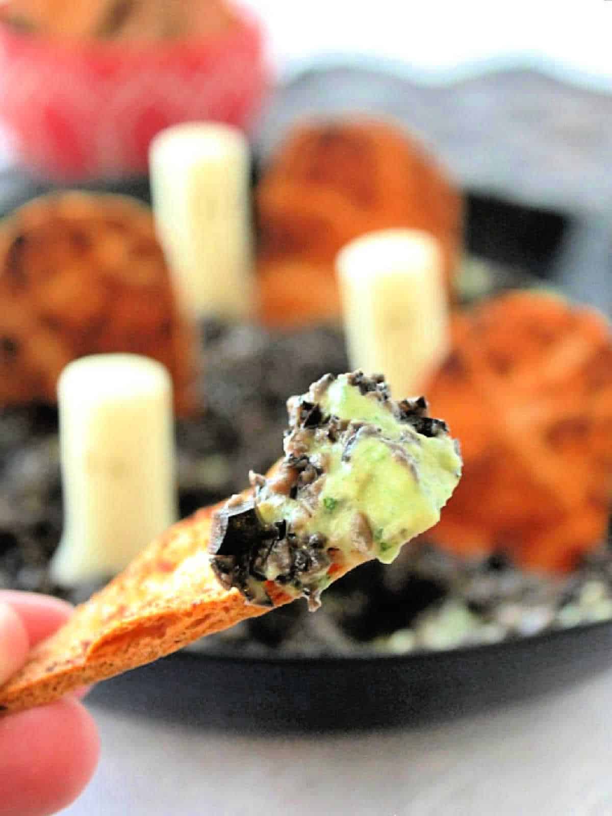 showing a homemade tortilla chip being dipped into the halloween dip