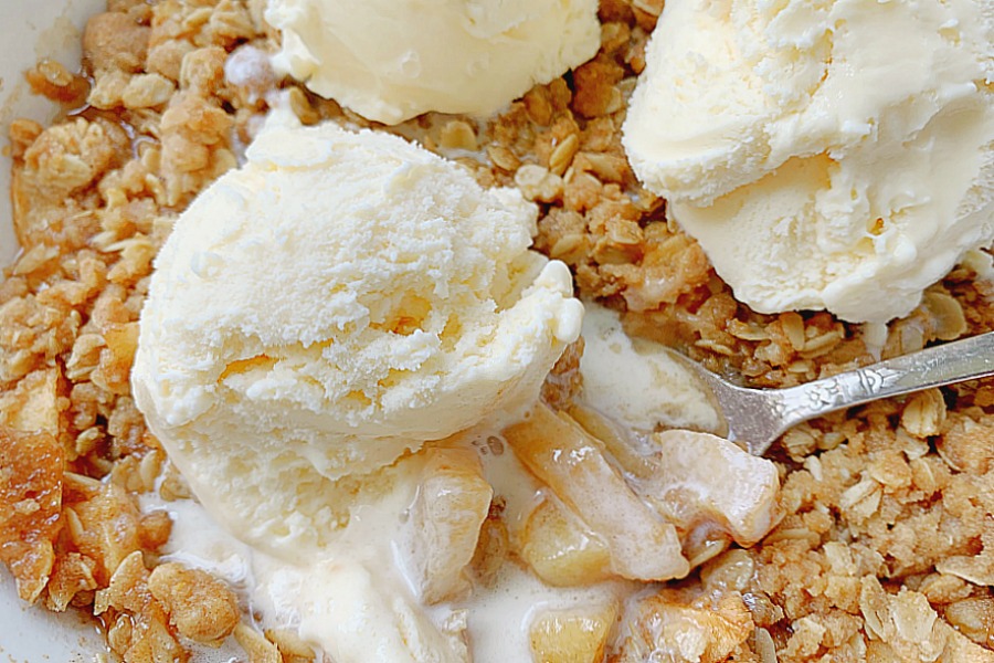 scooping out apple crisp topped with vanilla ice cream