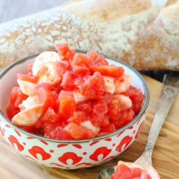 a decorative bowlful of canned tomato bruschetta on a board with baguette slices