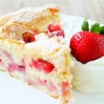 plated slice of french strawberry cake, garnished with whipped cream and a whole fresh strawberry
