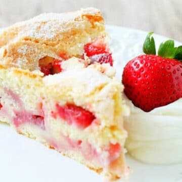 plated slice of french strawberry cake, garnished with whipped cream and a whole fresh strawberry