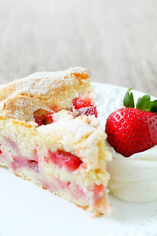 slice of french strawberry cake on plate with whole strawberry and whipped cream