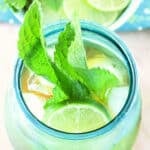 a turquoise glass of mojito iced tea garnished with a lime slice and fresh mint leaves