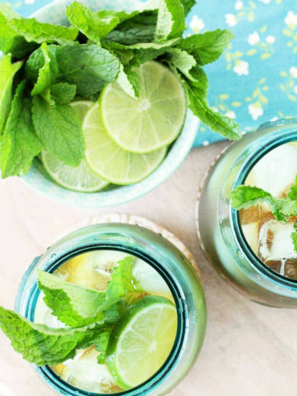 overhead picture of mojito iced tea glasses alongside a bowl of fresh lime slices and mint leaves