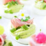 a close up photo of a deviled egg garnished with chopped green onions and a slice of prosciutto