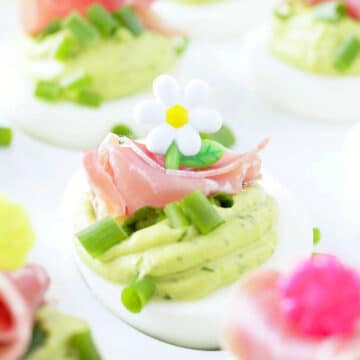 a close up photo of a deviled egg garnished with chopped green onions and a slice of prosciutto