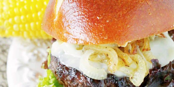 Grilled bourbon burger on a plate with a pretzel bun and an ear of corn on the cob