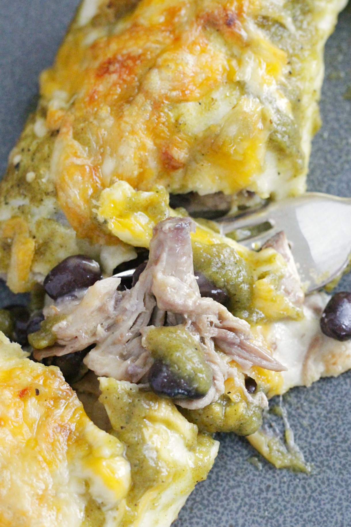 close up of individual pork enchilada on gray plate with fork