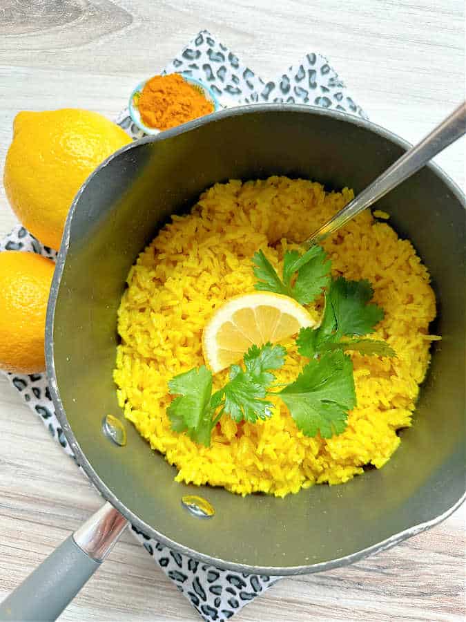 cooked turmeric rice in a nonstick sauce pan garnished with lemon and cilantro