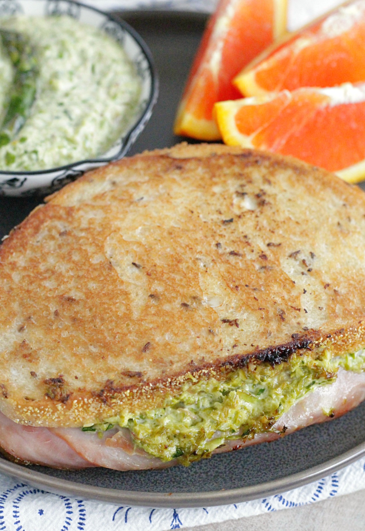 top view of whole grilled ham and cheese sandwich with asparagus mayonnaise on plate with orange slices