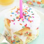 plated stack of funfetti pancakes topped with vanilla glaze, sprinkles and a pink candle