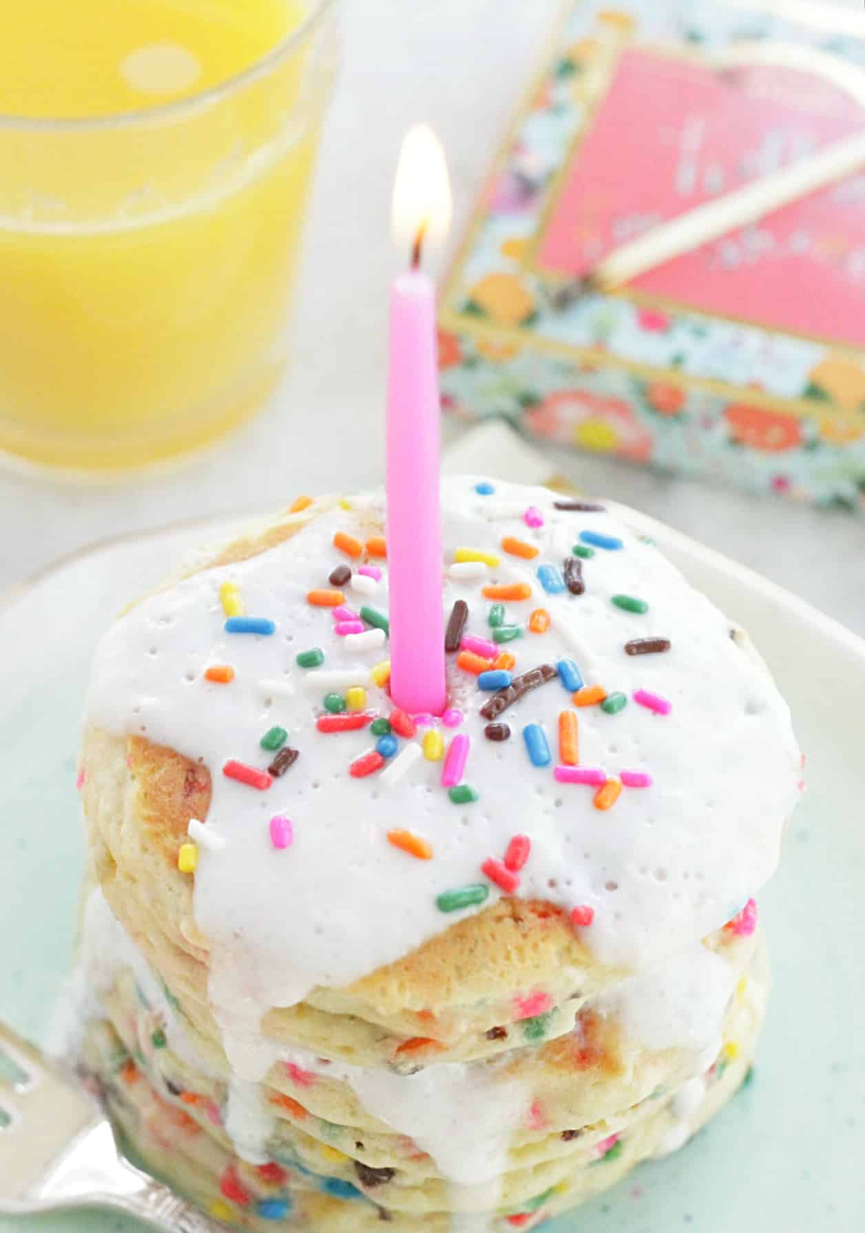 plated funfetti pancakes topped with vanilla glaze, sprinkles and a pink candle