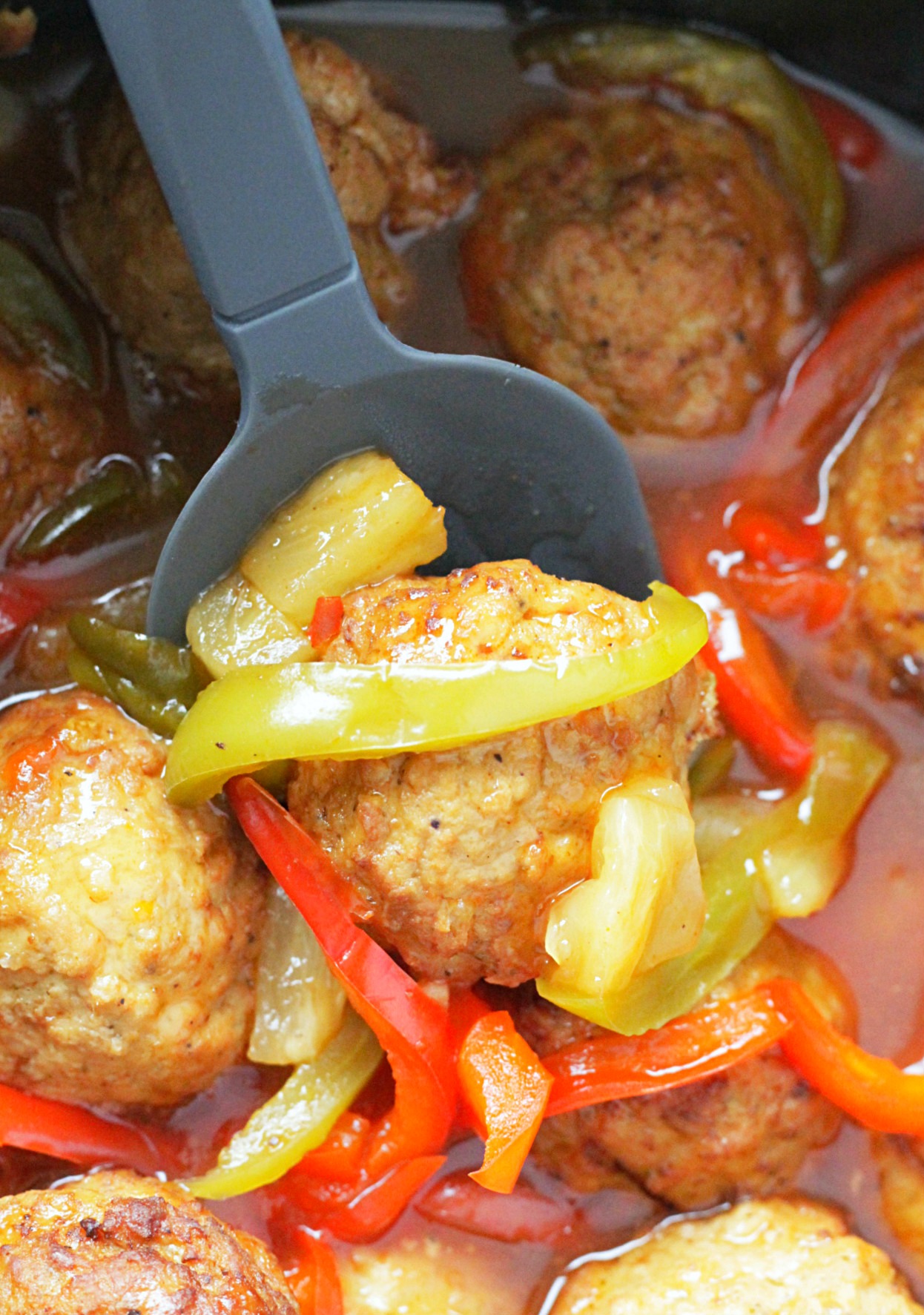 slow cooker sweet and sour meatballs in the crockpot with a spoon