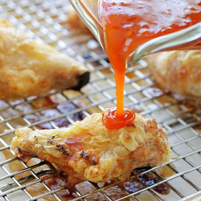 sauce being poured over the crispy baked chicken wings