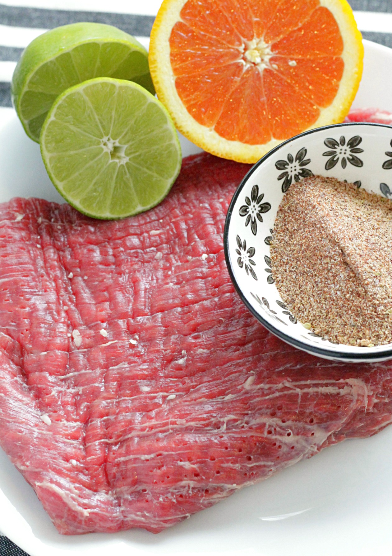 grilled carne asada burrito bowls - raw flank steak on cutting board with sliced orange and lime and dry rub