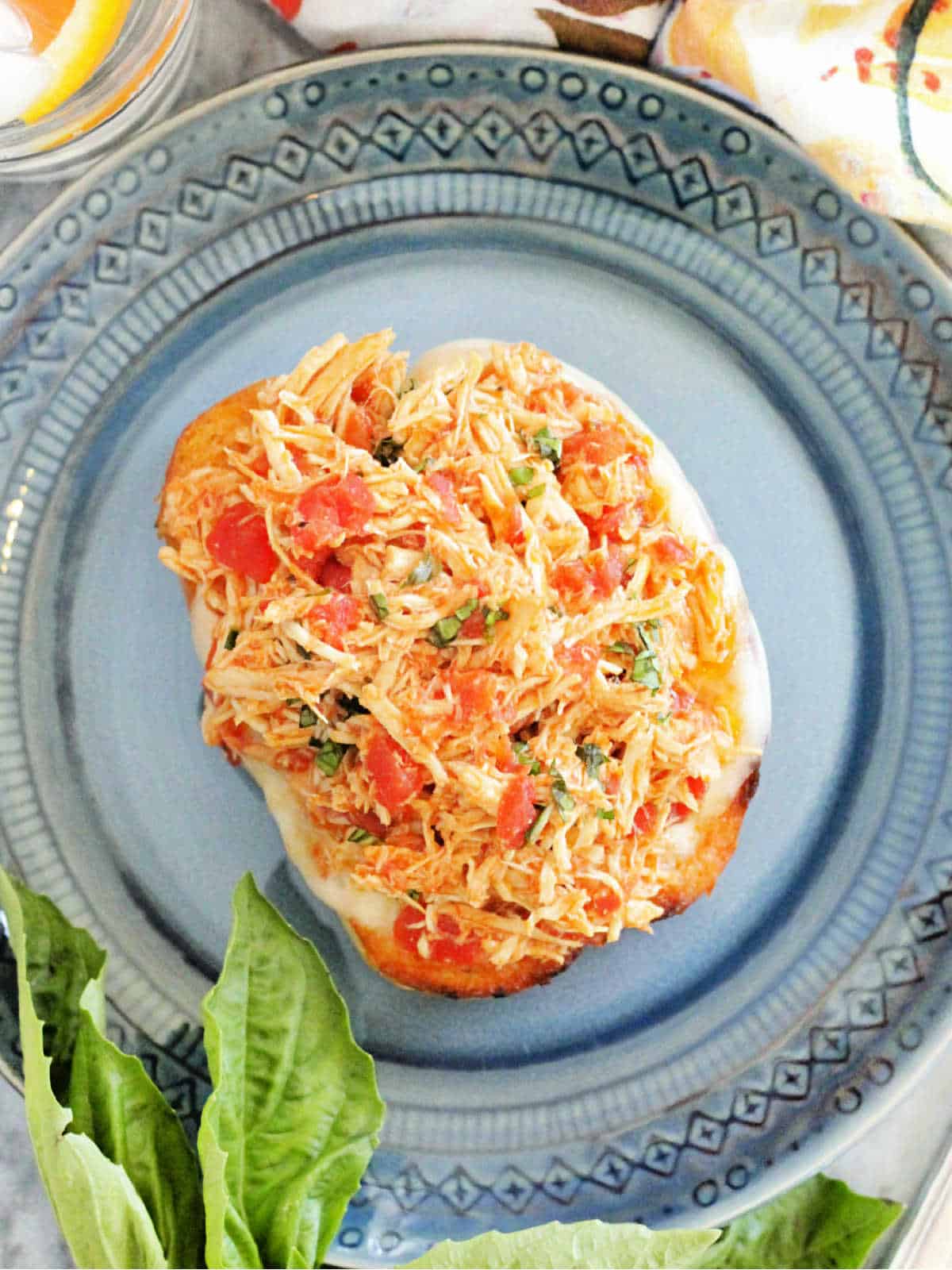 open faced crockpot chicken sandwich on a blue plate and garnished with fresh basil