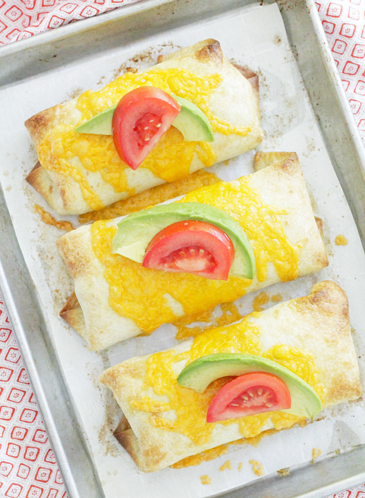 oven fried chimichangas overhead baked on sheet pan and topped with fresh tomato and avocado