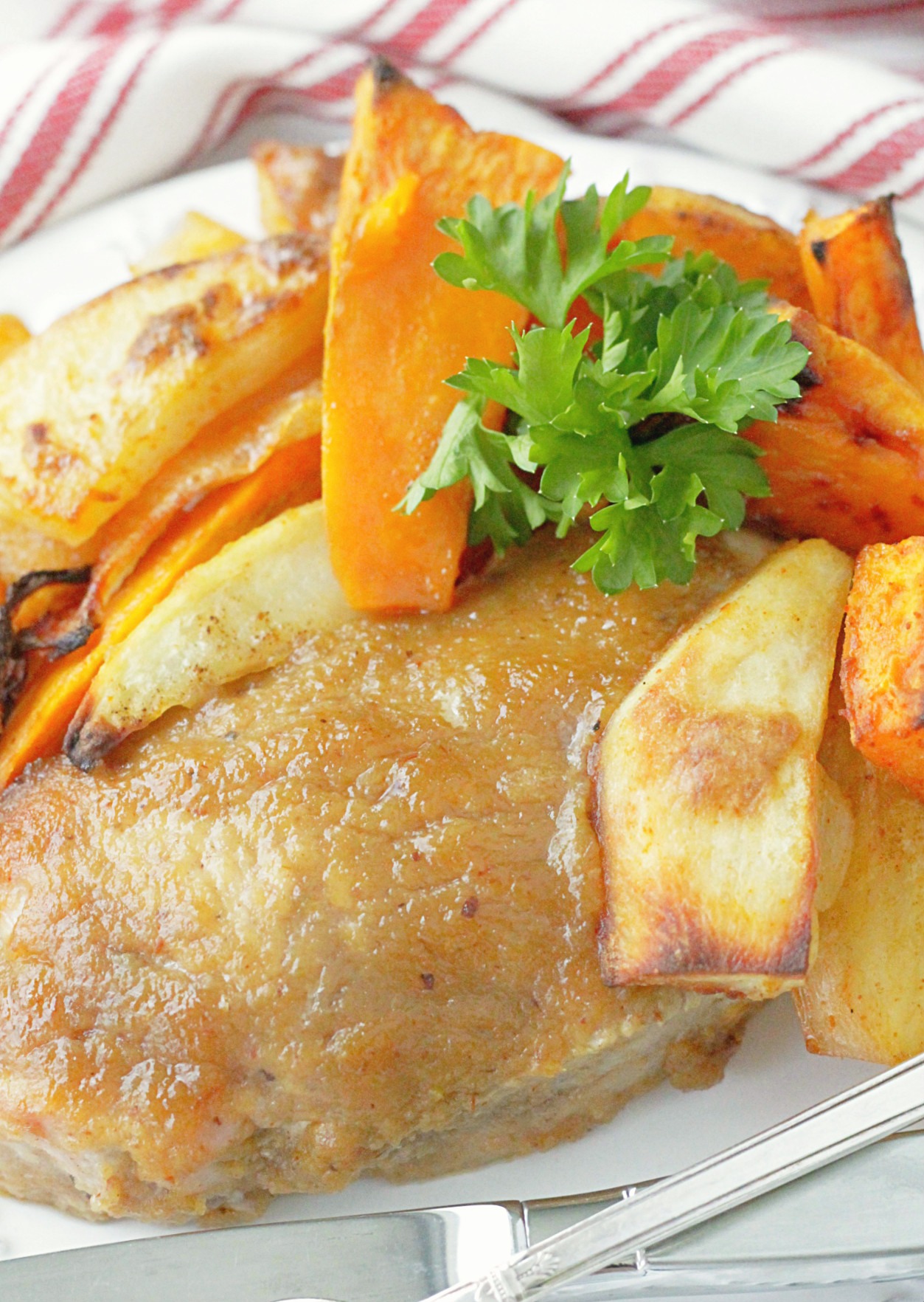 close up of applesauce baked pork chop on a plate with roasted potatoes