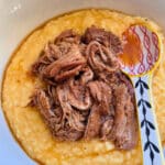 a bowl of cheddar cheese grits topped with apple butter glazed pulled pork