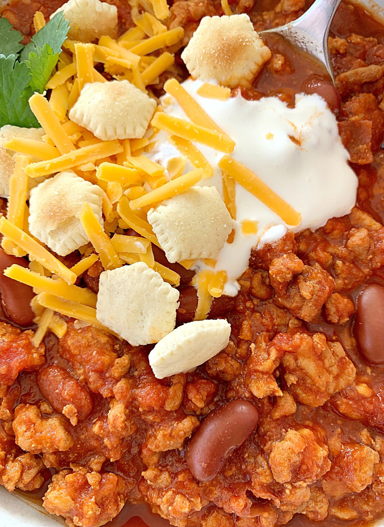 close up view of crockpot turkey chili topped with sour cream, oyster crackers and shredded cheese