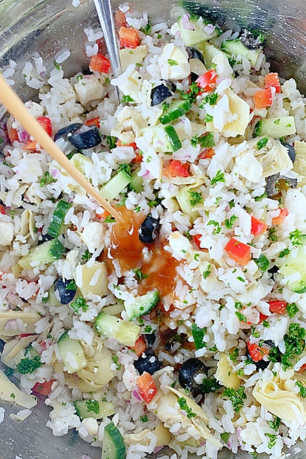 dressing being poured onto greek rice salad