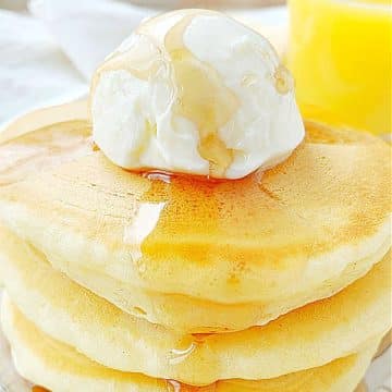a stack of three fluffy buttermilk pancakes topped with butter and maple syrup