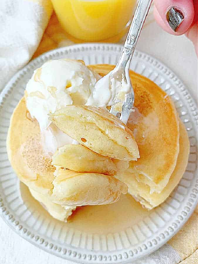 taking a big bite of buttermilk pancakes that have been covered in butter and maple syrup