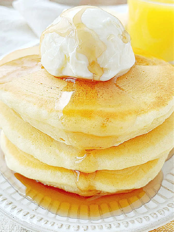 a stack of perfect buttermilk pancakes topped with a scoop of butter and pure maple syrup