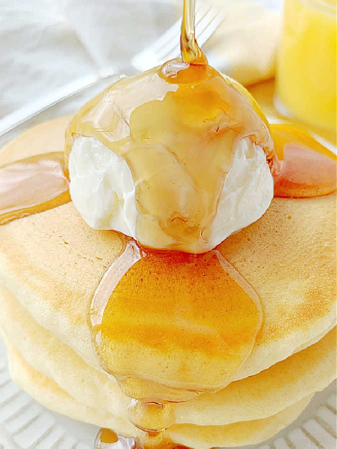 pouring maple syrup over a stack of three fluffy buttermilk pancakes