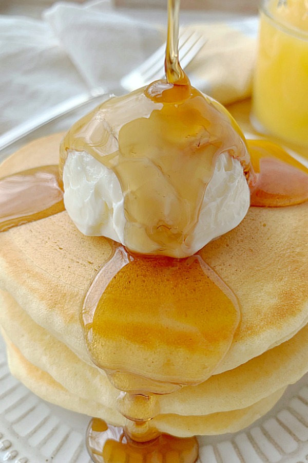 stack of buttermilk pancakes with syrup being poured on them