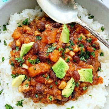 a bowl of vegetarian chili over white rice and garnished with fresh avocado