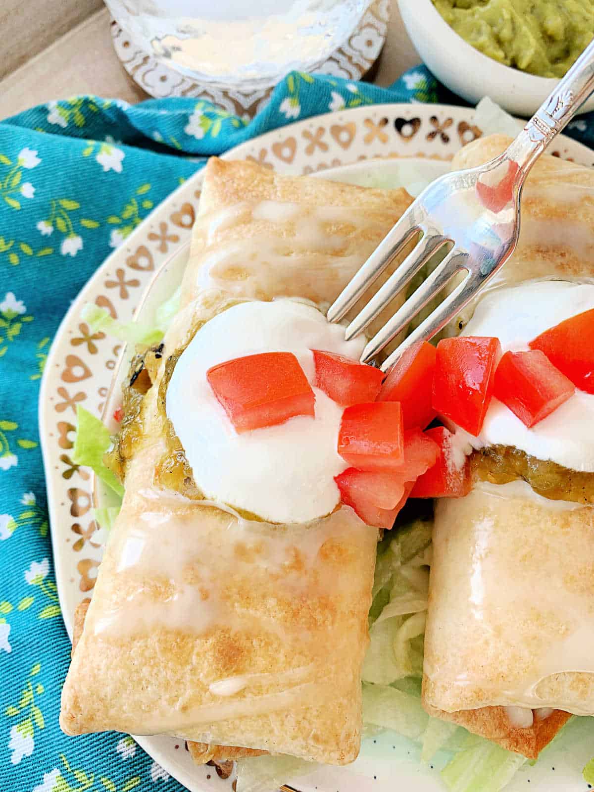 two plated air fryer chicken chimichangas garnished with queso, sour cream and tomatoes
