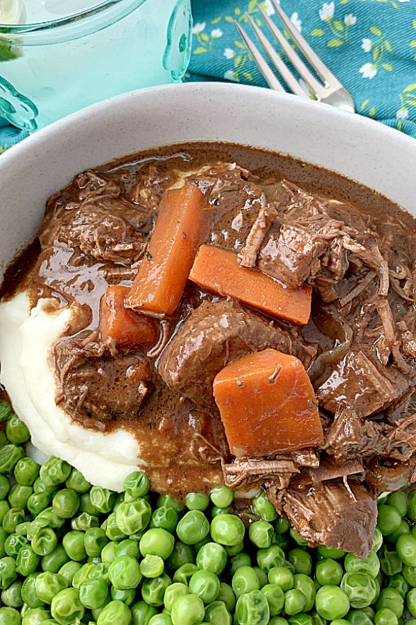 guinness beef stew in bowl with mashed potatoes and peas