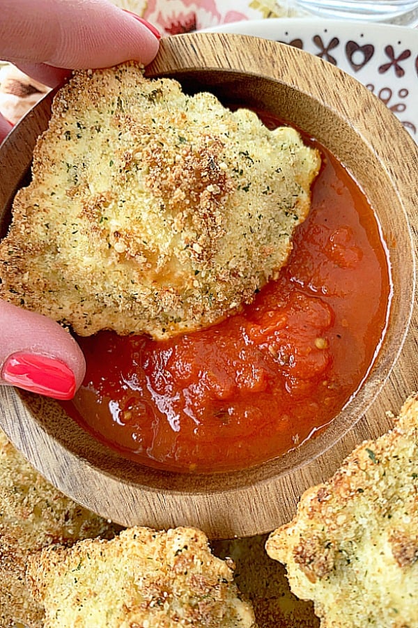 air fryer ravioli being dipped into bowl of marinara sauce