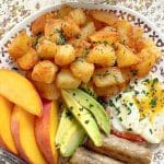 plated breakfast potatoes with sliced peaches, fried egg, sausage and avocado