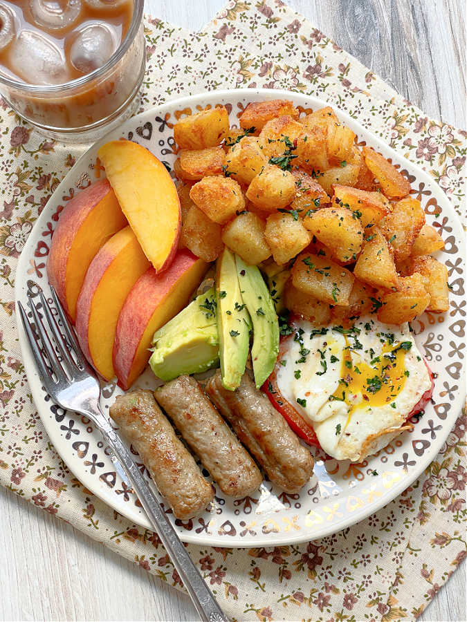 breakfast potatoes plated with fresh peaches, fried egg and chicken sausage