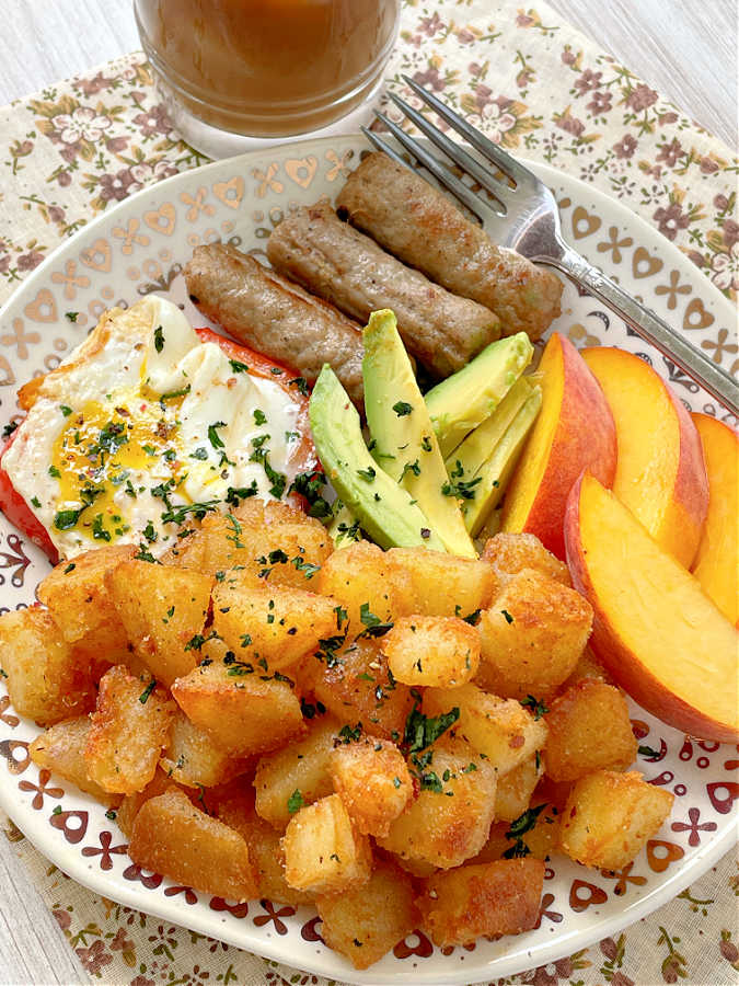 focusing on the breakfast potatoes plated with a fried egg, peaches, avocado and sausage
