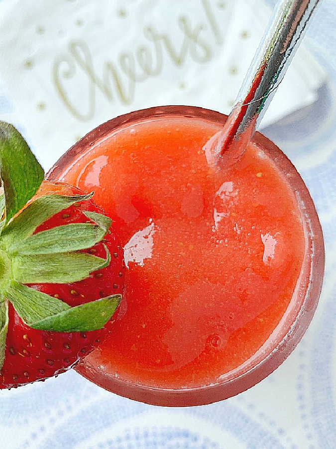 a frosty glass full of frozen strawberry daiquiri, garnished with a shiny silver straw and a large fresh strawberry