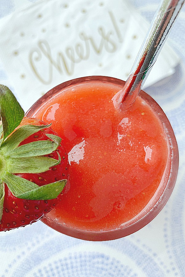 glass of strawberry daiquiri with cheers napkins